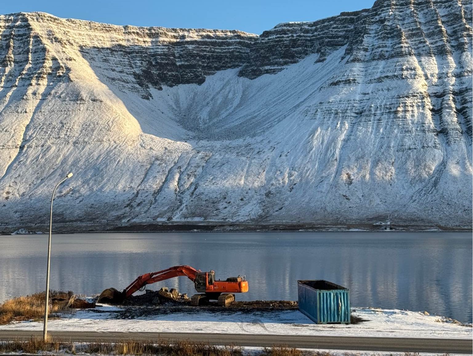 Gamla Grænagarðsbryggjan séð frá hjólagarðinum ofan við Skutulsfjarðarbraut. Á bryggjunni er grafa og í baksýn er Naustahvilft. Það er bjartur haustdagur og þunnt lag af snjó liggur yfir öllu.